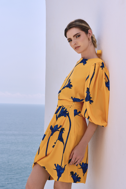 A model wearing a yellow top with blue flowers and a bow detail on the back; and a yellow skirt with blue flowers by Monica Arguedas