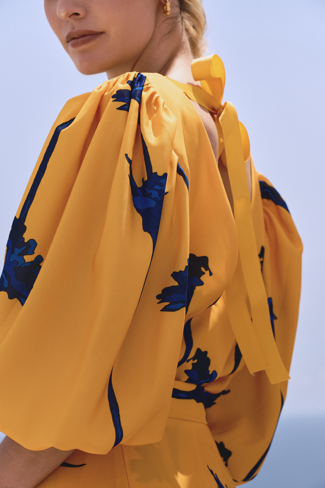 A model wearing a yellow top with blue flowers and a bow detail on the back by Monica Arguedas