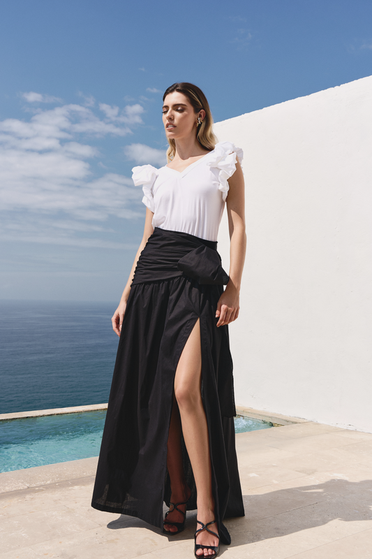 A model wearing a solid black skirt with a bow and slit by Monica Arguedas