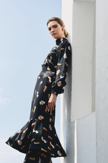 A model wearing a black long-sleeve top and black ruffled skirt with floral print by Monica Arguedas