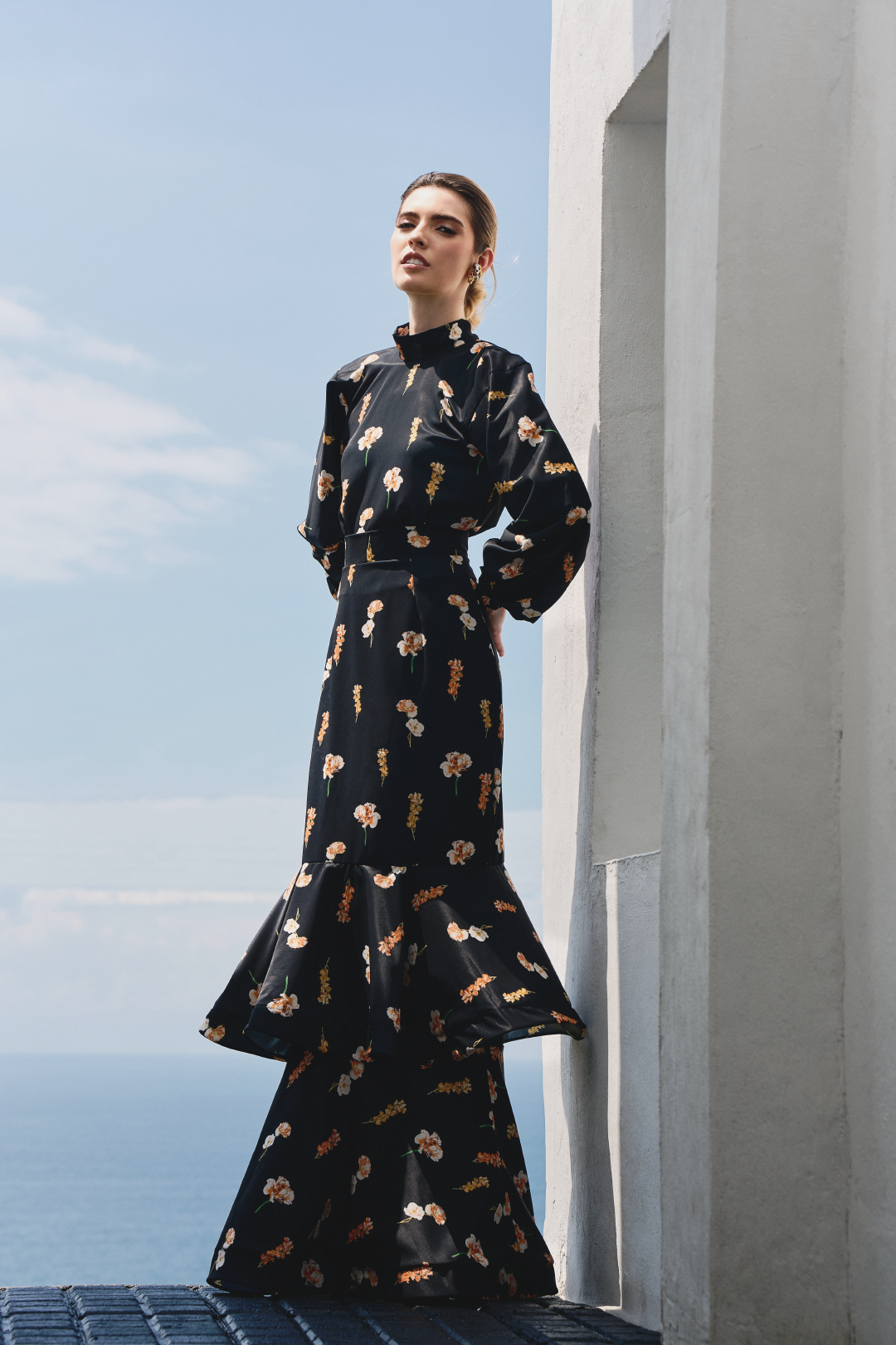A model wearing a black long-sleeve top and black ruffled skirt with floral print by Monica Arguedas