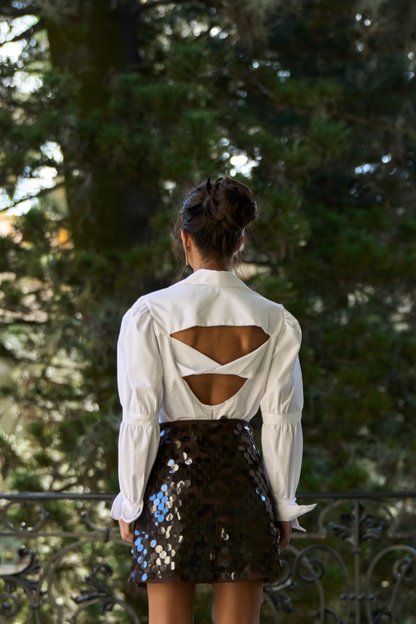 A model wearing a white blouse with an open back and scrunched sleeves.