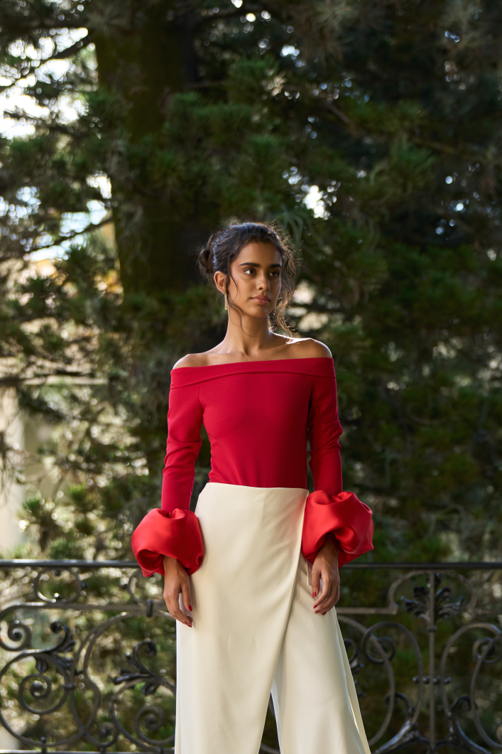A model wearing a red off the shoulder bodysuit with long sleeves and a puffy wrist detail by Monica Arguedas.