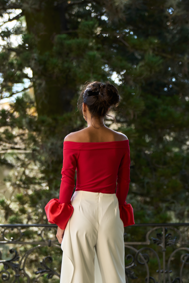 A model wearing a red off the shoulder bodysuit with long sleeves and a puffy wrist detail by Monica Arguedas.